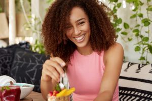 mulher-encaracolada-de-expressao-alegre-come-deliciosa-sobremesa-esta-de-bom-humor-passa-o-tempo-em-aconchegante-cafeteria-aprecia-saborosa-salada-de-frutas-mulher-atraente-descansando-sozinha-apos-a-excursao